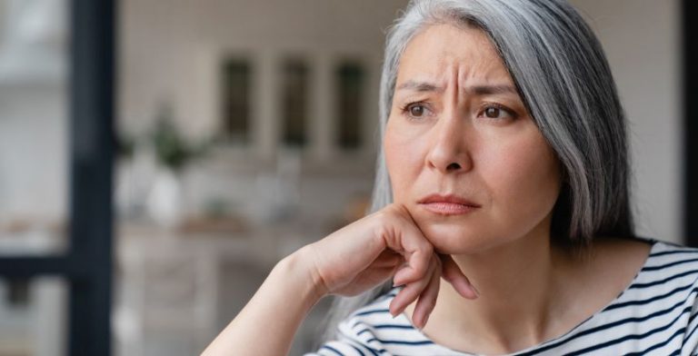 An older woman sitting with her head resting on the back of her hand. She is wearing a black and white striped shirt and has greying hair.