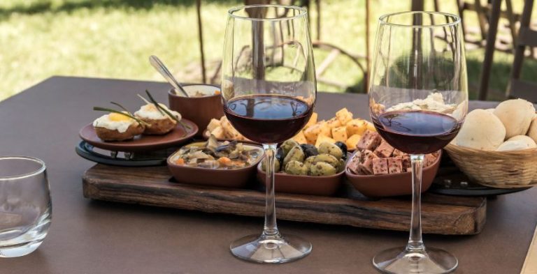 A table with two glasses of red wine and appetizers in the background.