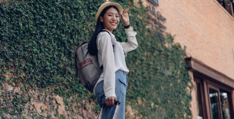 A woman with a backpack standing in front of a building covered in ivy.