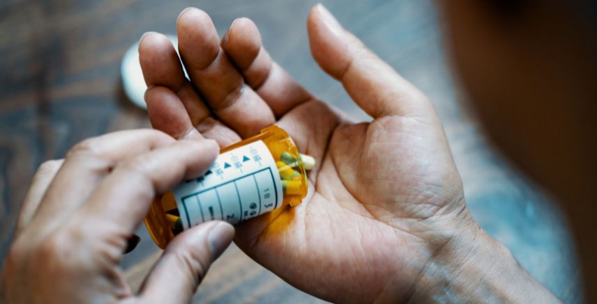 A hand emptying a prescription bottle of pills into their other open hand.