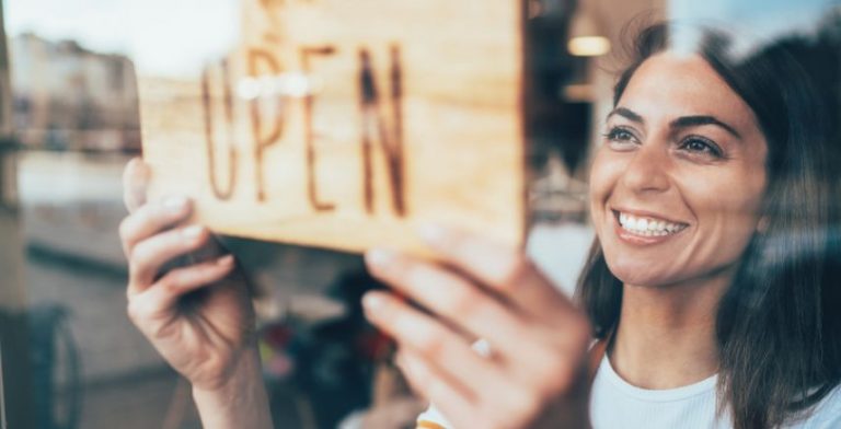 A woman putting up an "OPEN" sign in a shop window.