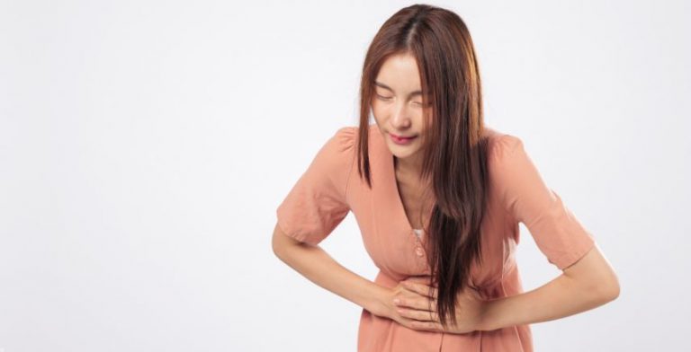 A woman in a pink dress, bent over holding her stomach as if in pain.
