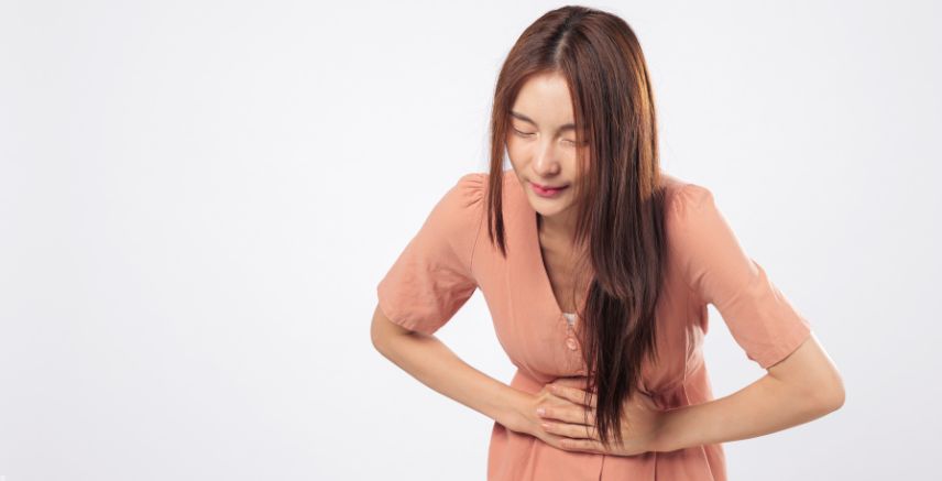 A woman in a pink dress, bent over holding her stomach as if in pain.